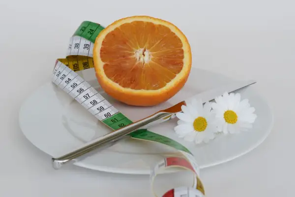 Pomarańcza na talerzu z miarką krawiecką i kwiatami symbolizuje zdrową dietę odchudzającą.