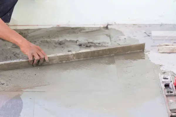 Ręka wyrównuje świeży beton, tworząc idealnie gładką podłogę na gruncie.