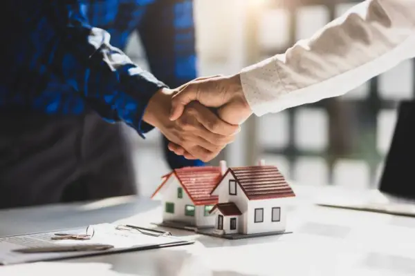 Poignée de main sur des maquettes de maisons, symbolisant un accord. Le compromis de vente délai dépassé par le vendeur est une préoccupation.