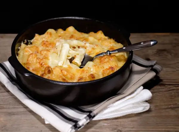 Un plat réconfortant de gratin de pâtes à l'ancienne, doré et gratiné au fromage, servi dans un plat noir avec une cuillère.