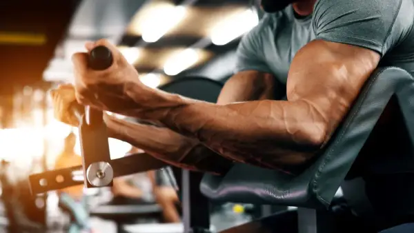 Ein Mann trainiert seinen Bizeps-Muskel an einem Gerät im Fitnessstudio. Die Adern treten deutlich hervor.