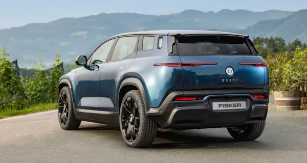 Tylna część niebieskiego elektrycznego SUV-a Fisker Ocean na tle gór i zieleni.