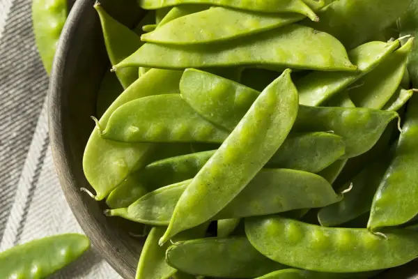 Un bol en bois rempli de pois gourmands frais, prêts pour la cuisson.