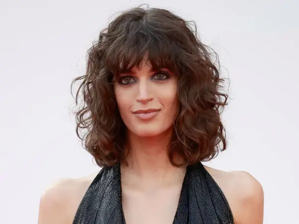 Mujer con curly pelo corto rizado natural, mirada intensa y vestido negro brillante.