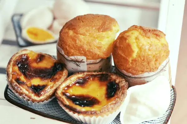 Pyszne portugalskie ciastka, w tym dwa kremowe pastel de nata i dwa muffinki, kuszą apetycznym wyglądem.