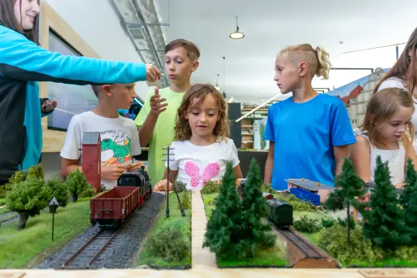 Dzieci oglądają makietę kolejową z pociągami i budynkami.