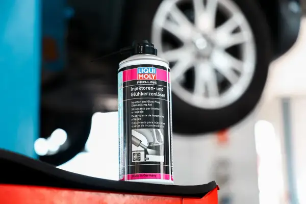 Puszka preparatu do czyszczenia wtryskiwaczy Liqui Moly na tle koła samochodu. Pomaga w demontażu zapieczonych elementów.
