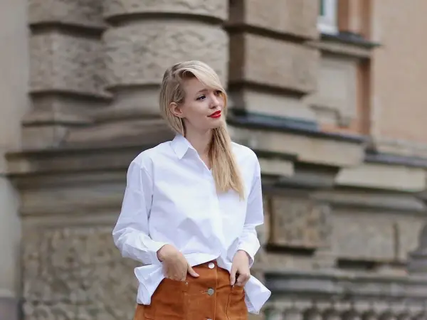 Mujer con falda de gamuza y camisa blanca, posando con las manos en los bolsillos.