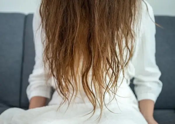 Cabello castaño, con puntas secas y aspecto de pelo quemado, cayendo sobre una bata blanca.