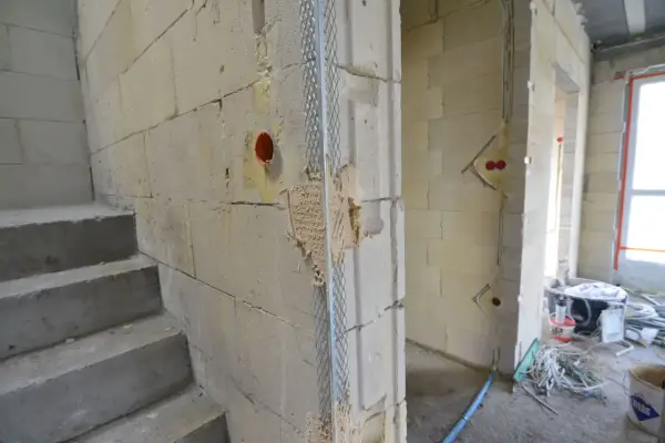 Schody betonowe, ściany z bloczków, instalacja elektryczna i siatka na tynk. Widać postęp prac na budowie.