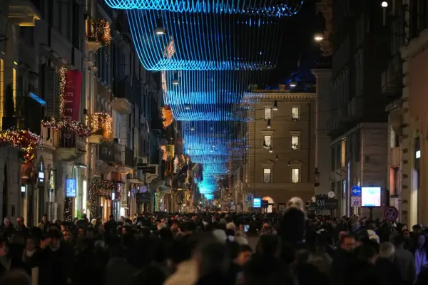 Folla festosa in strada a Roma, 25 dicembre, sotto luminarie blu e decorazioni natalizie.