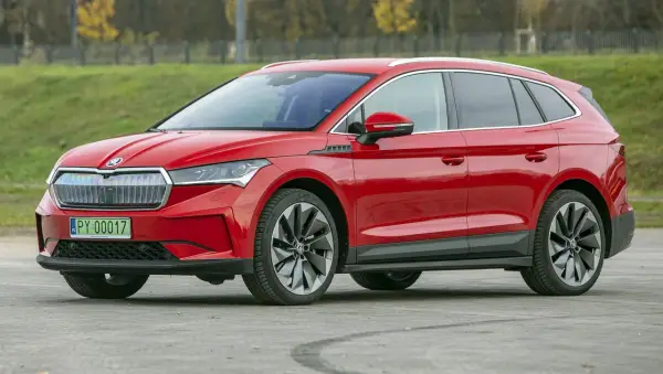 Czerwona Skoda Enyaq na tle zieleni. Sprawdź aktualną skoda enyaq cena i wybierz swój wymarzony samochód elektryczny.