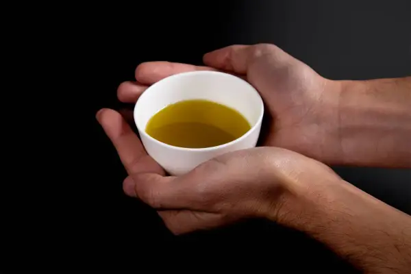 Mani che sorreggono una tazzina bianca con olio evo. Il suo significato è prezioso, un nettare dorato.