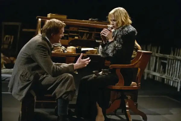 Una scena intensa da Dogville recensione: un uomo parla animatamente a una donna seduta, che tiene una tazza tra le mani.