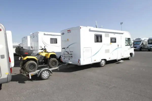 Un quad jaune sur une remorque, prêt à être tracté par un camping-car. Le quad est bien attaché, prêt pour l'aventure, comme indiqué sur la carte grise.
