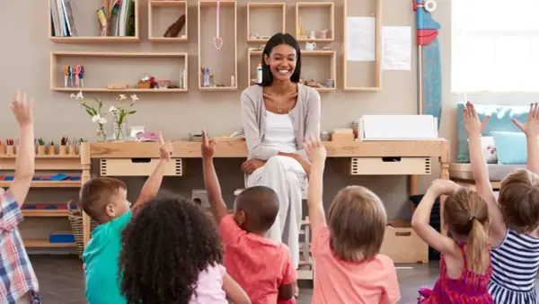 Niños en un aula **Waldorf Montessori** levantan las manos para responder a su maestra sonriente.