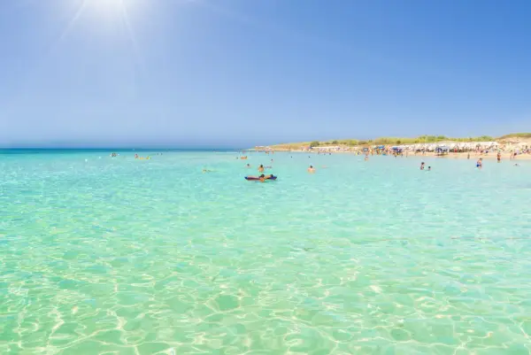 Crystal clear turquoise waters and a sandy beach with sunbathers, perfect for those wondering where to stay in Puglia for beaches.