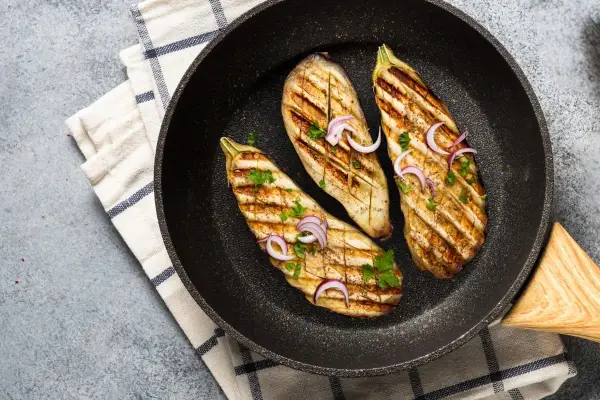 Aubergines grillées dans une poêle, garnies d'oignons rouges et de persil. Une délicieuse recette aubergine prête à être dégustée.