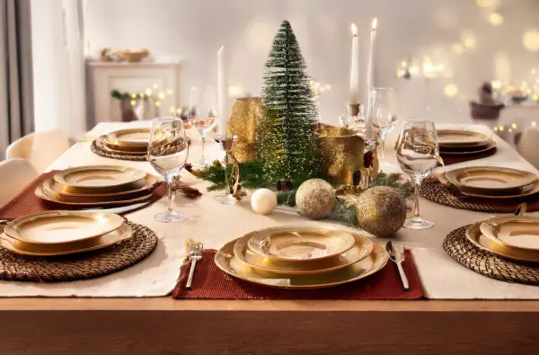 Table dressée pour un repas festif, avec une **fourchette à la française** posée sur une serviette rouge, des assiettes dorées et un centre de table de Noël.