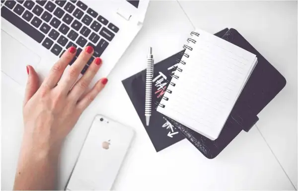 Karta pracy na biurku: dłoń na klawiaturze laptopa, obok telefon, notatnik i długopis.