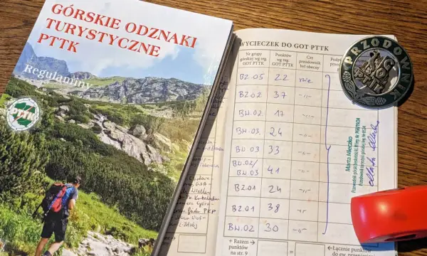 Książeczka GOT PTTK z wpisami wycieczek i odznaką przodownika.