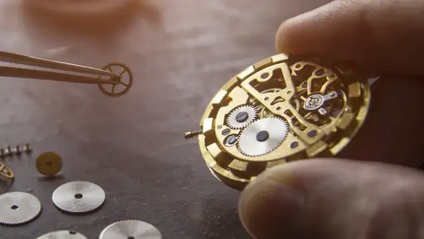 Un orologiaio assembla i componenti di un orologio meccanico, mostrando ingranaggi e molle dorate.