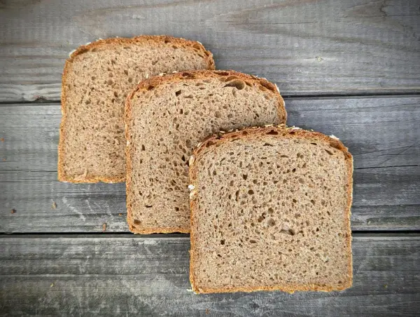 Drei Scheiben **Vollkornbrot** aus der **Kastenform** liegen auf rustikalem Holz.
