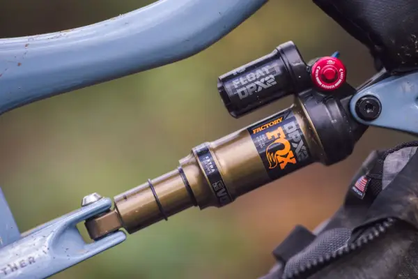 Close-up of a blue bicycle frame with a gold and black Fox Float DPX2 Factory shock. The shock has "FACTORY" and "DPX2" branding.