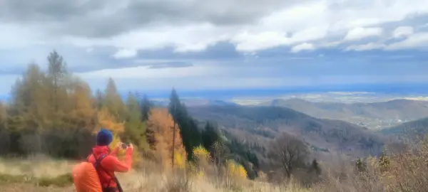 Widok na Beskid Mały jesienią. Turysta z pomarańczowym plecakiem fotografuje panoramę.