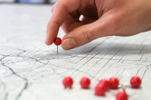 Una mano coloca un alfiler rojo sobre un mapa, marcando puntos clave para planificar rutas de aprendizaje y explorar nuevas posibilidades.