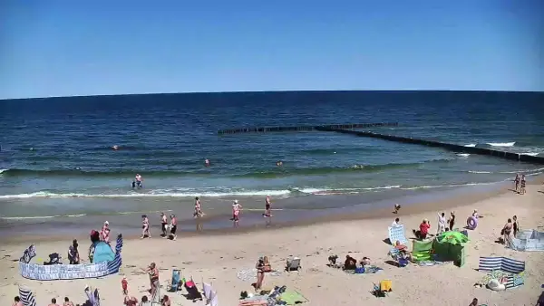 Słoneczna plaża w Dźwirzynie, ludzie kąpią się w morzu i odpoczywają na piasku. To jedne z wielu atrakcji tego miejsca.