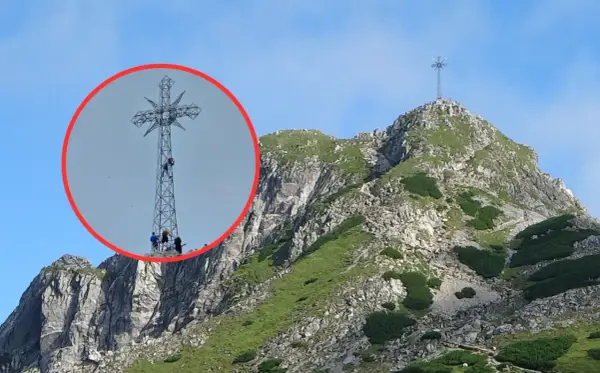 Ludzie wspinają się na krzyż na Giewoncie. Czy krzyż na Giewoncie świeci? Widać go z daleka na tle błękitnego nieba.