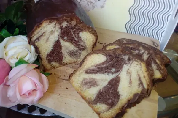 Wilgotna babka marmurkowa na oleju, oblana czekoladą, prezentuje się apetycznie obok róż.