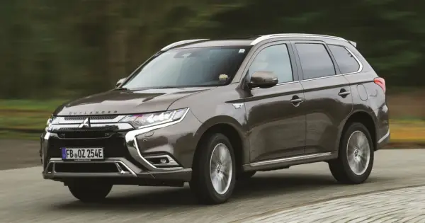 Brązowy Mitsubishi Outlander PHEV jedzie po drodze, z rozmytym tłem lasu.