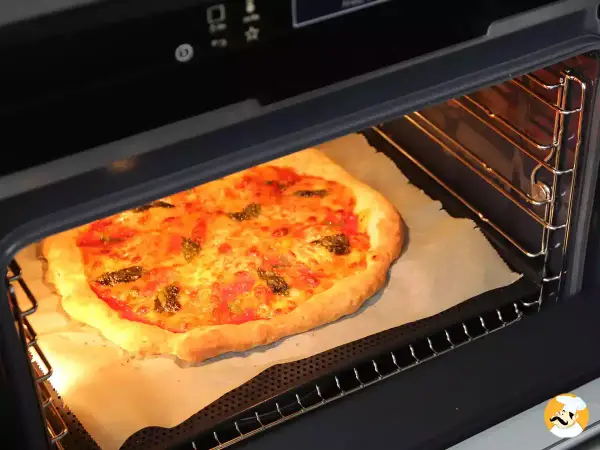 Une pizza maison dorée et appétissante cuit dans un four, prête à être dégustée. Une parfaite recette pizza au four.