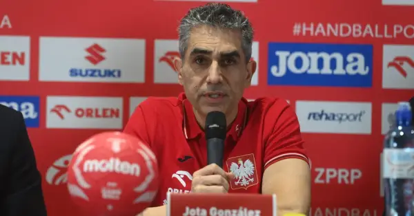 Jota González, trener reprezentacji Polski w piłce ręcznej, przemawia do mikrofonu. Obok niego czerwona piłka.