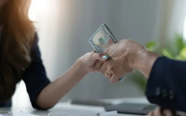 Dwie ręce przekazują sobie plik banknotów. To symboliczny moment zawarcia umowy pożyczki.