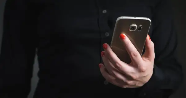Dłoń z czerwonymi paznokciami trzyma telefon, szukając informacji, jak zablokować SMS premium.