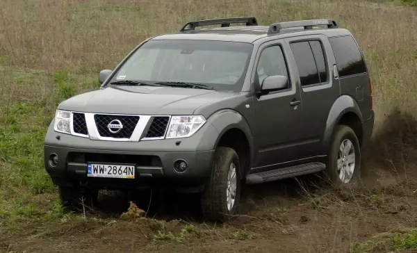 Szary Nissan Pathfinder r51 pokonuje błotniste wzniesienie, wzbijając tumany kurzu.