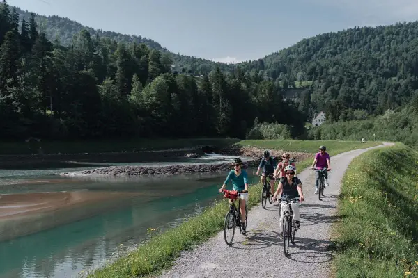 Gruppe genießt MTB Touren entlang eines Flusses mit bewaldeten Hügeln im Hintergrund.