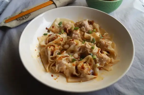 Pyszne ciasto wonton w pikantnym sosie, posypane szczypiorkiem i sezamem. Obok pałeczki w etui.