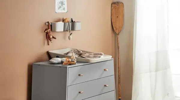Eine Wickelkommode organisieren: Spielzeug, Handtücher und Pflegeutensilien sind ordentlich verstaut. Ein Holzpaddel lehnt an der Wand.