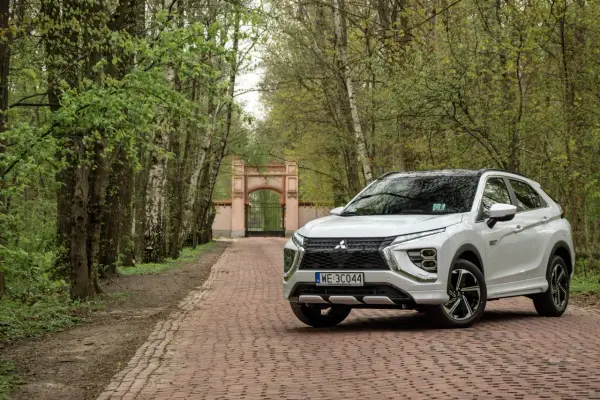 Biały Mitsubishi Eclipse Cross na tle bramy i drzew. Wiele pozytywnych mitsubishi eclipse cross opinie potwierdza jego wszechstronność.