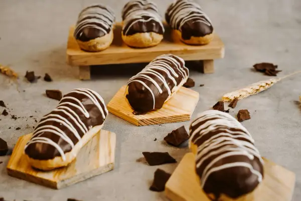 Éclairs gourmands avec un glaçage éclair chocolat brillant, décorés de fines rayures blanches. Des éclats de chocolat parsèment la table.