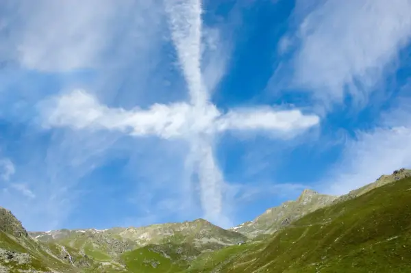 Ein Kreuz aus Wolken am blauen Himmel über grünen Bergen. Man könnte sagen, ihr werdet Zeichen am Himmel sehen.