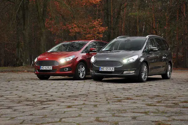 Dwa samochody Ford, czerwony S-Max i szary Galaxy, stoją na brukowanej nawierzchni w jesiennym lesie.