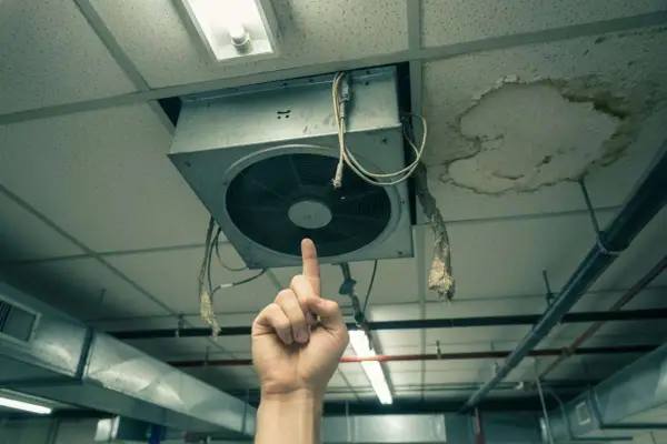Une main pointe un VMC bruyant au plafond, à côté d'une tache d'humidité.
