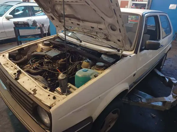 Biały Volkswagen Golf z otwartą maską, silnik gotowy do wyjęcia. Zastanawiasz się, ile kosztuje wyciągnięcie silnika?
