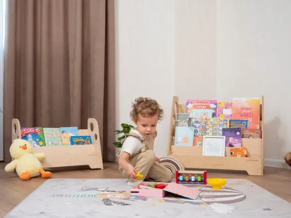 Kleines Kind spielt mit Holzspielzeug vor einem Regal mit Büchern, das eine Sitzordnung im Montessori-Stil widerspiegelt.