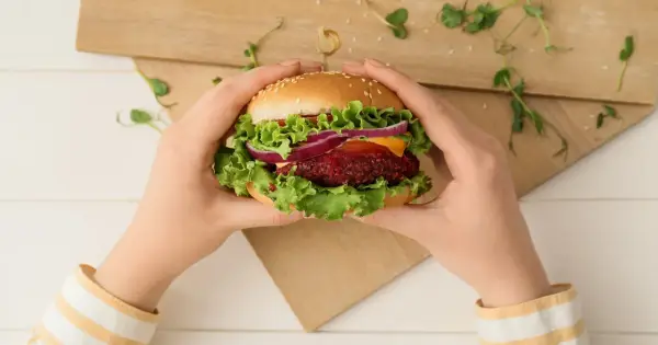 Ręce trzymają wegetariańskiego burgera z buraka, sałatą, cebulą i serem. Pyszna krowarzywa na desce.
